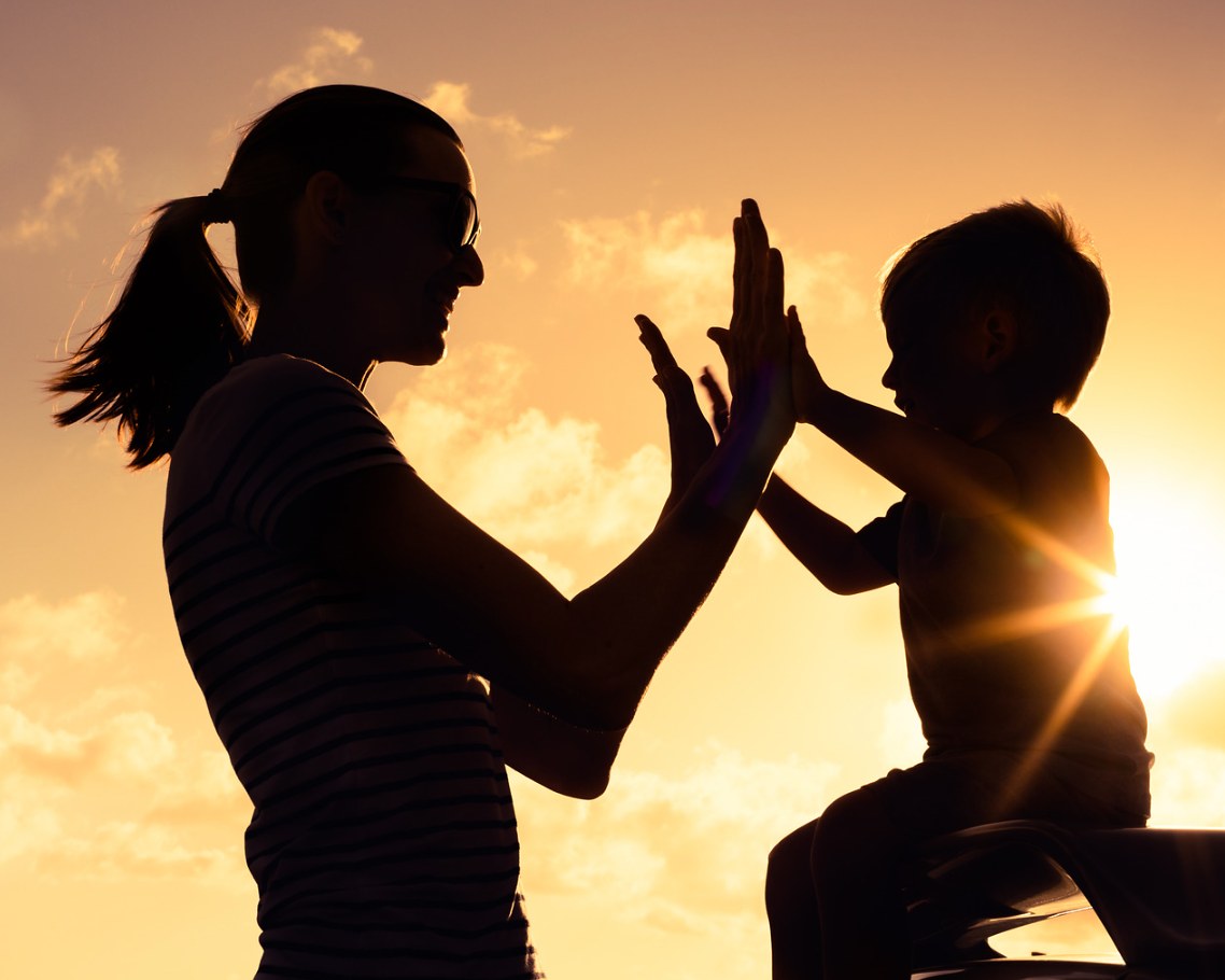 A parent and young child sharing a high-five at sunset