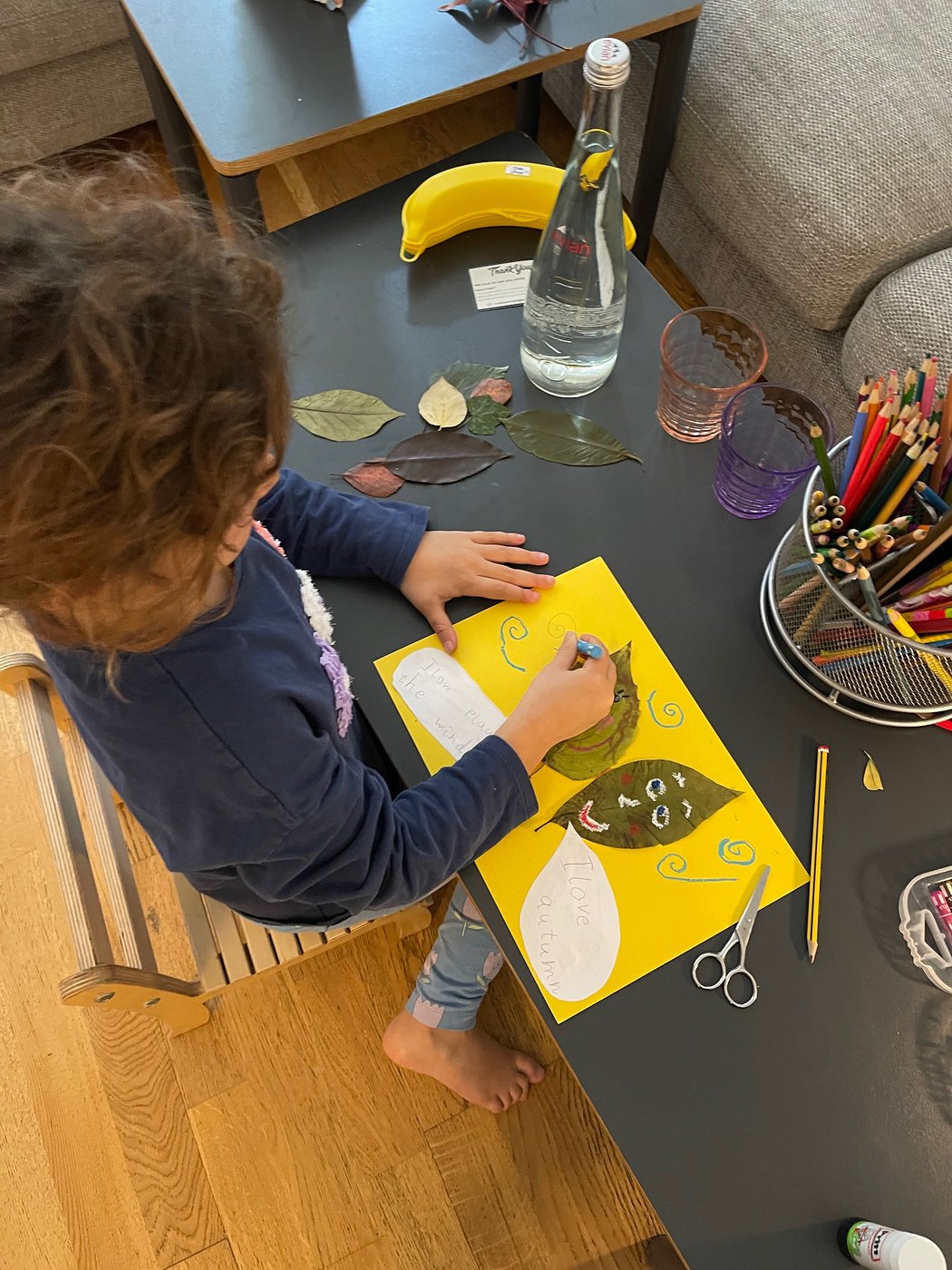 A child arranging leaves on yellow paper at a table